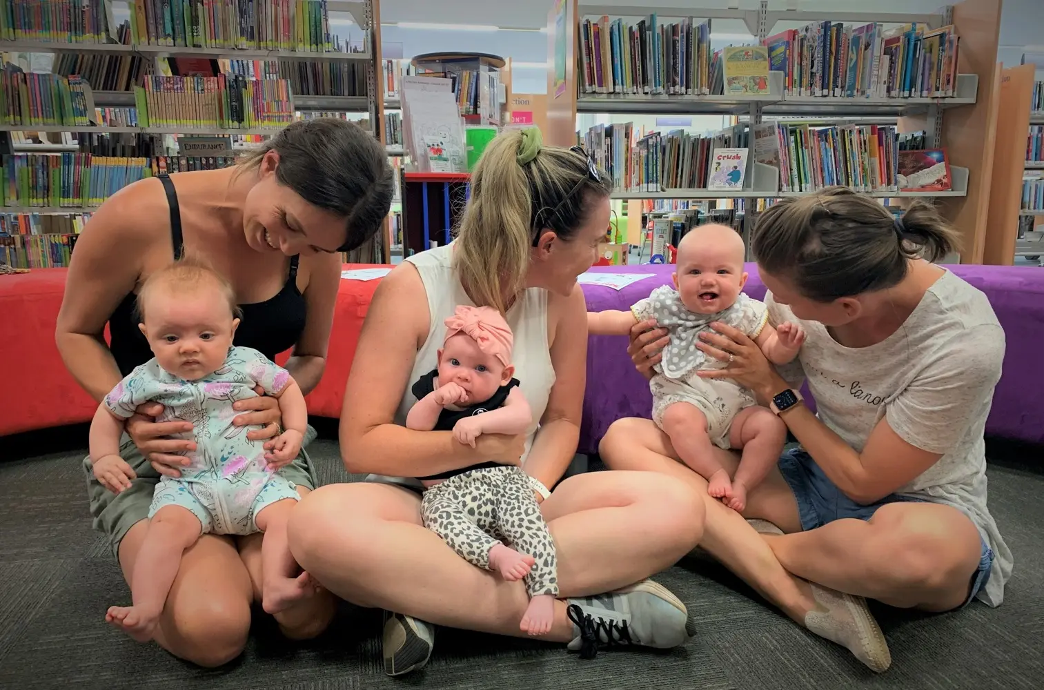 Three women sitting on the floor, holding babies.