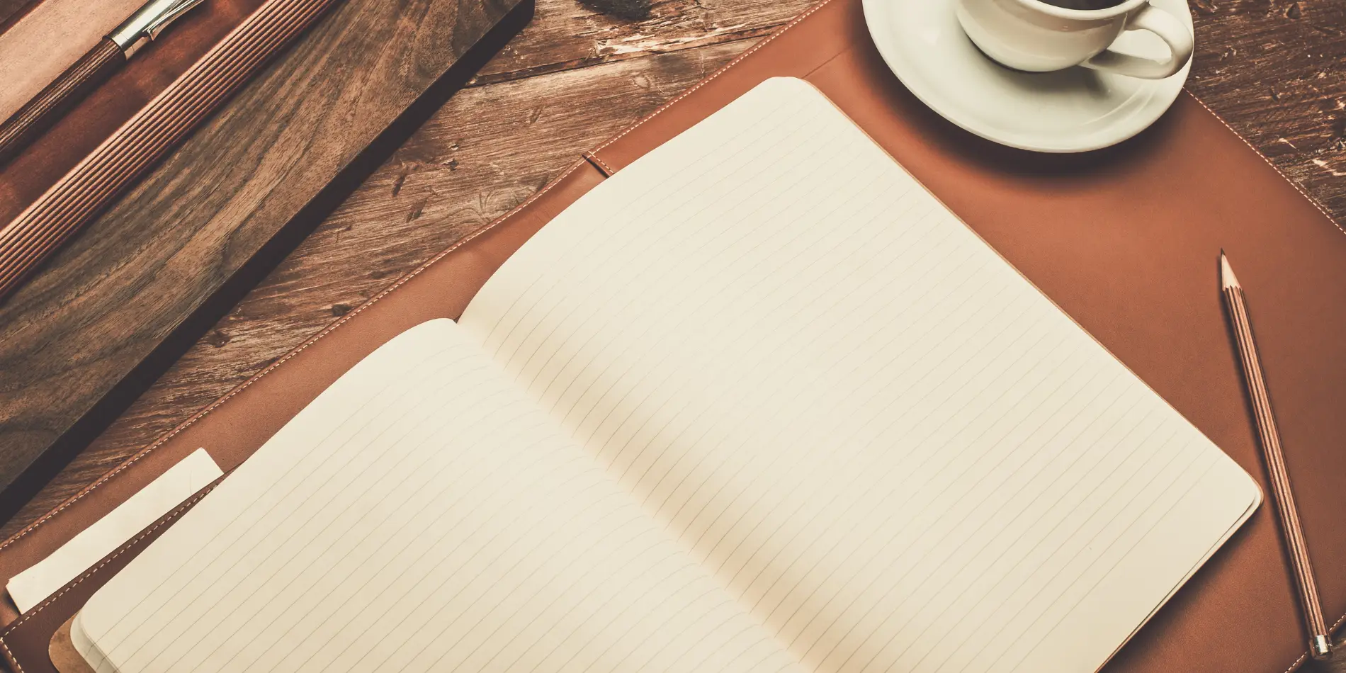 An open book with blank pages. A pencil and teacup are next to the book.