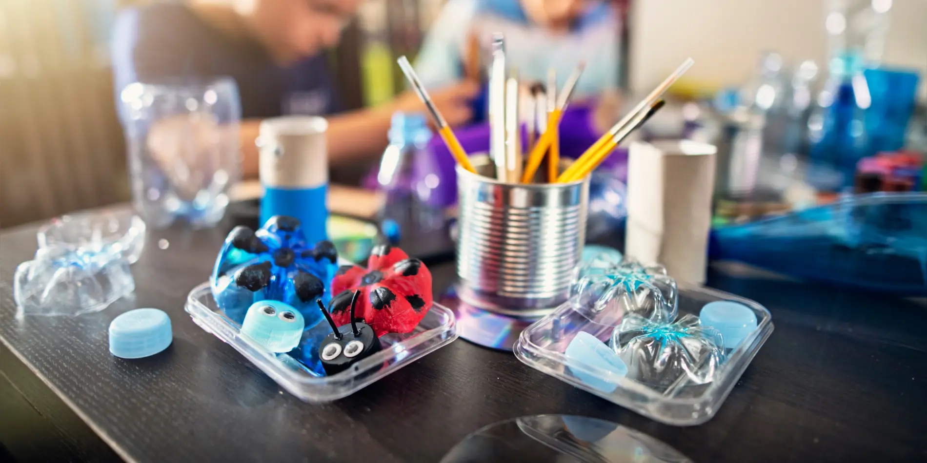 A table covered in craft supplies. Two children are in the background.