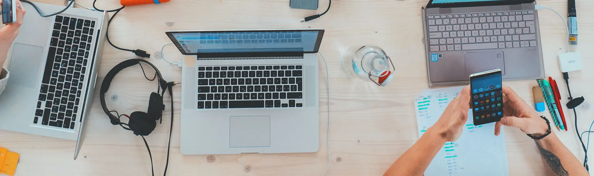 Three laptops open while two people look at phones.