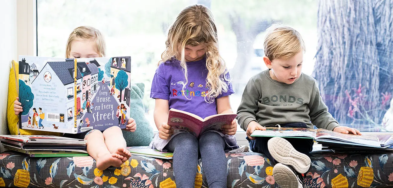 Three kids sitting down and reading books.