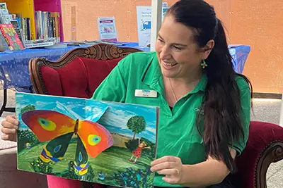 Seated woman holding a children's book open to be seen. A butterfly is on the page.