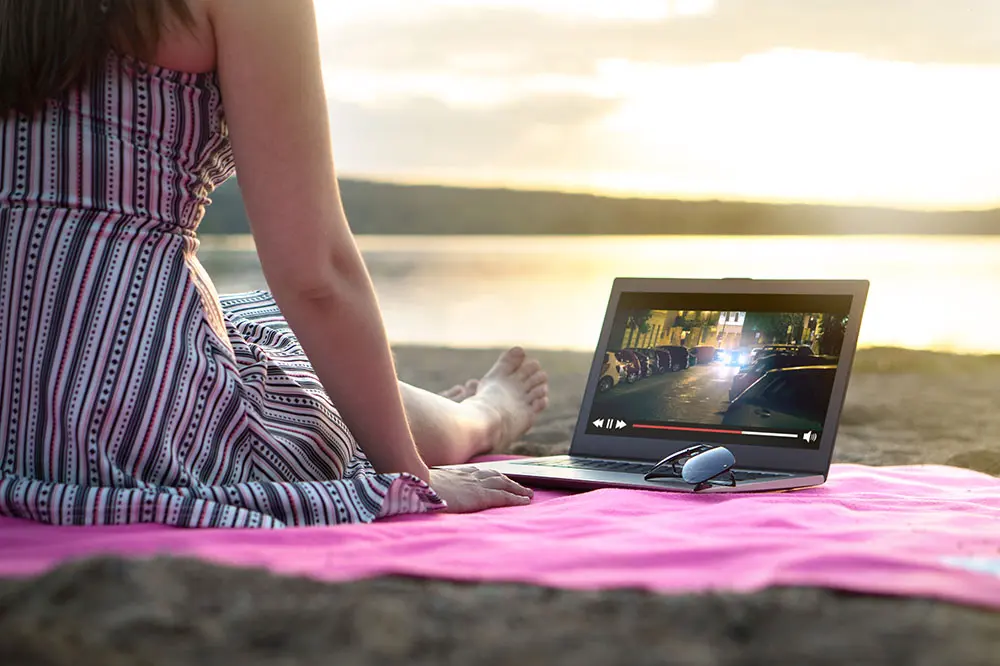 A woman watching a movie on a laptop while sitting on the beach.