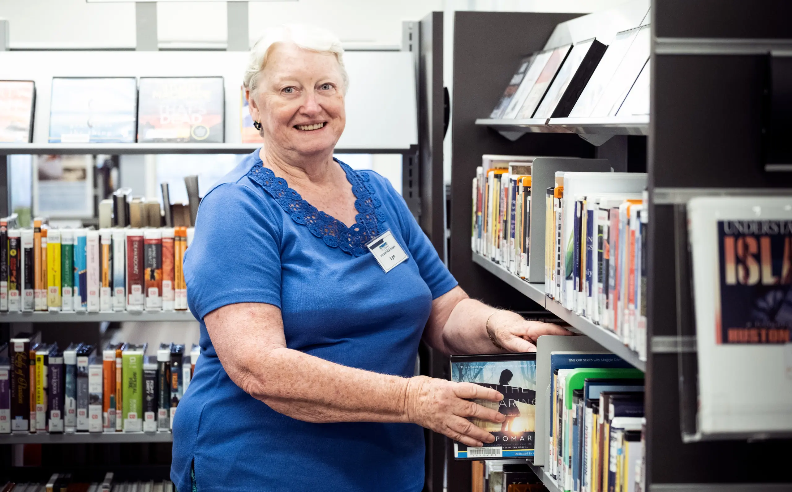 An older woman putting a DVD onto a library shelf.