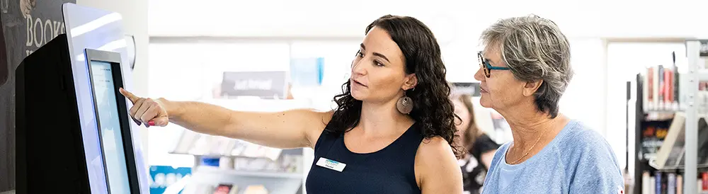 A librarian showing a library patron how to use the self-check-out.