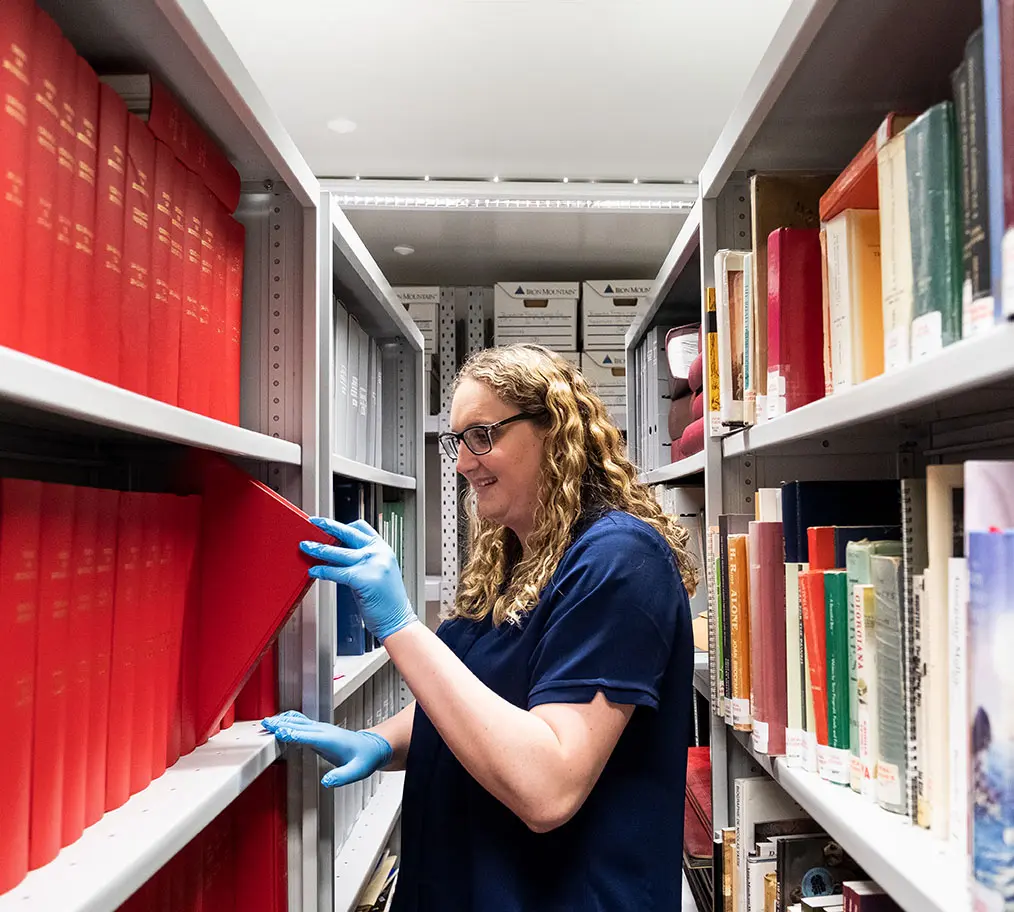 Woman between two bookshelves, taking a book from one.