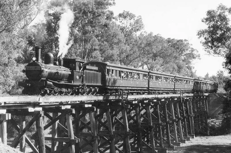 Black and white photo of a steam train going over a bridge.