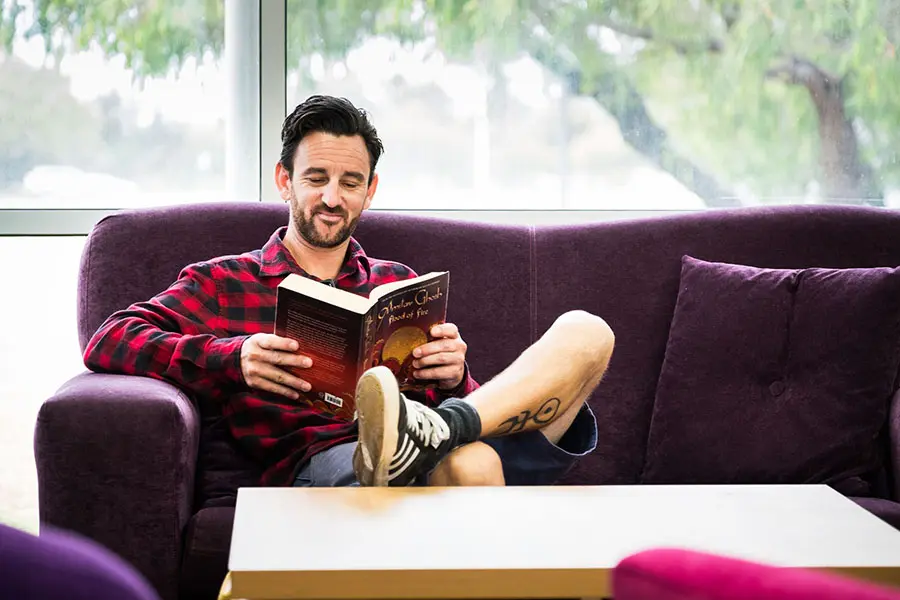 A man sitting on a lounge while reading a book.