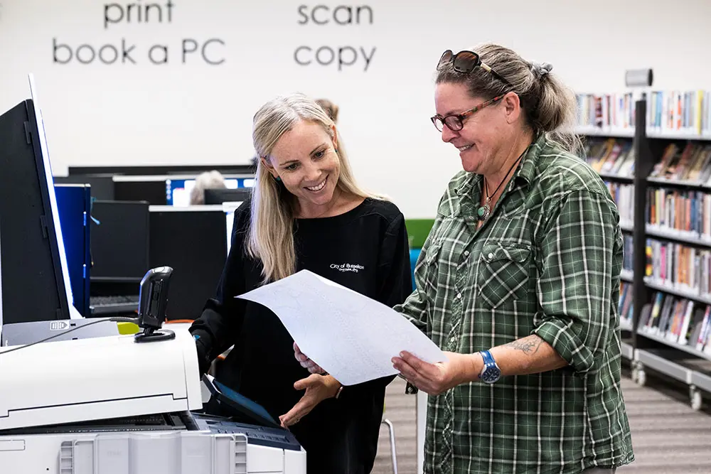 A librarian assisting a woman in using a photocopier.