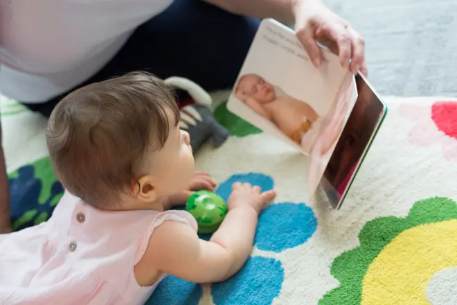 A baby looking at a book held open by an adult, sitting out of shot.
