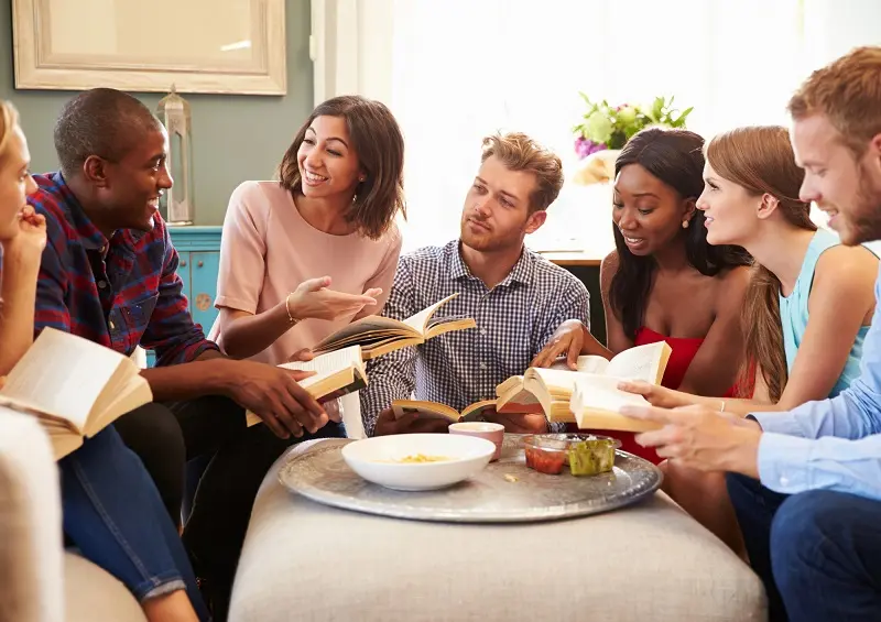 A group of people sitting around a table, each holding books.