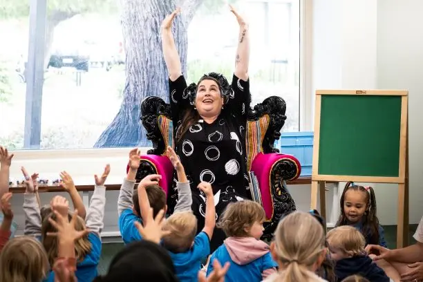 A woman surrounded by children, all with their arms raised.