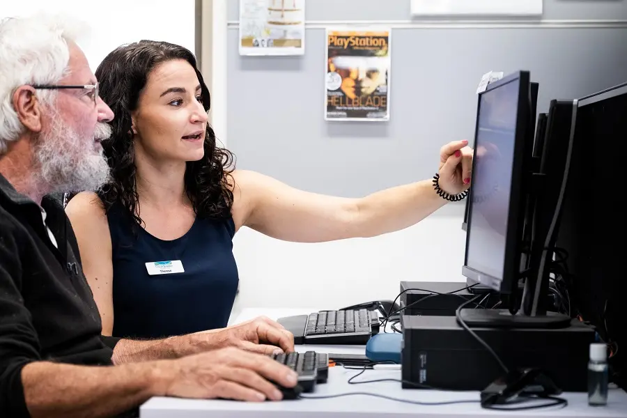 A young woman assisting an older man with using a computer.