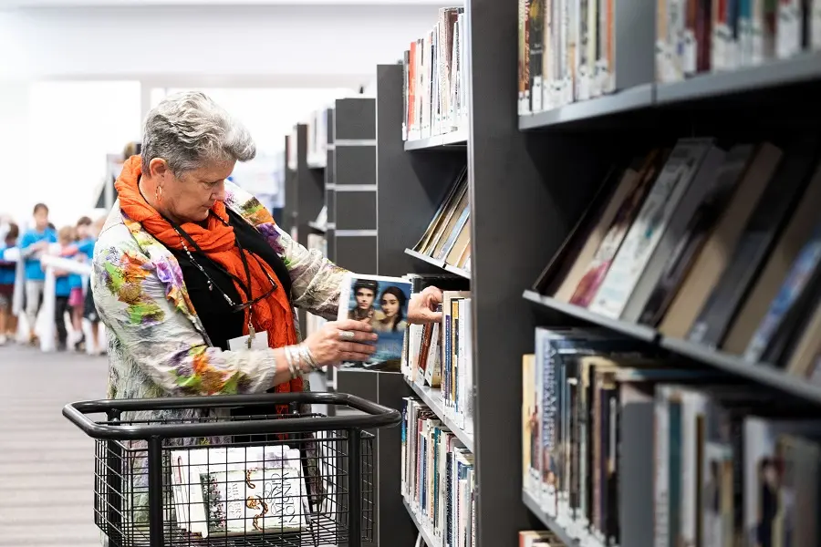 An older woman placing a book onto a library shelf.