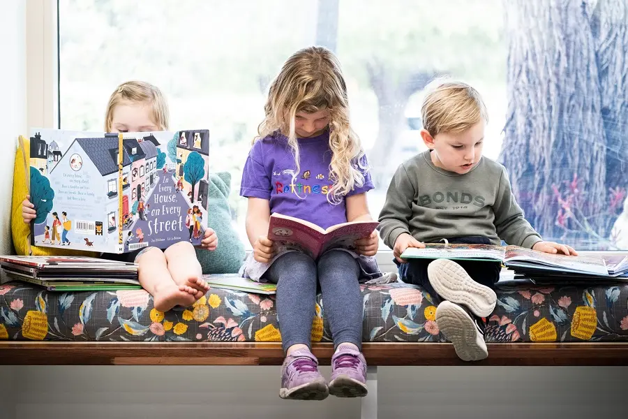 Three children seated together, each reading a different book.