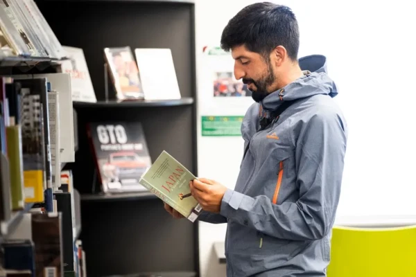 A man looking at a book, standing next to book shelves.
