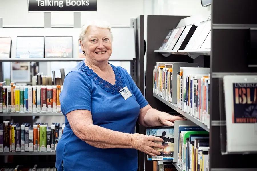 An older woman placing a DVD on a library shelf.