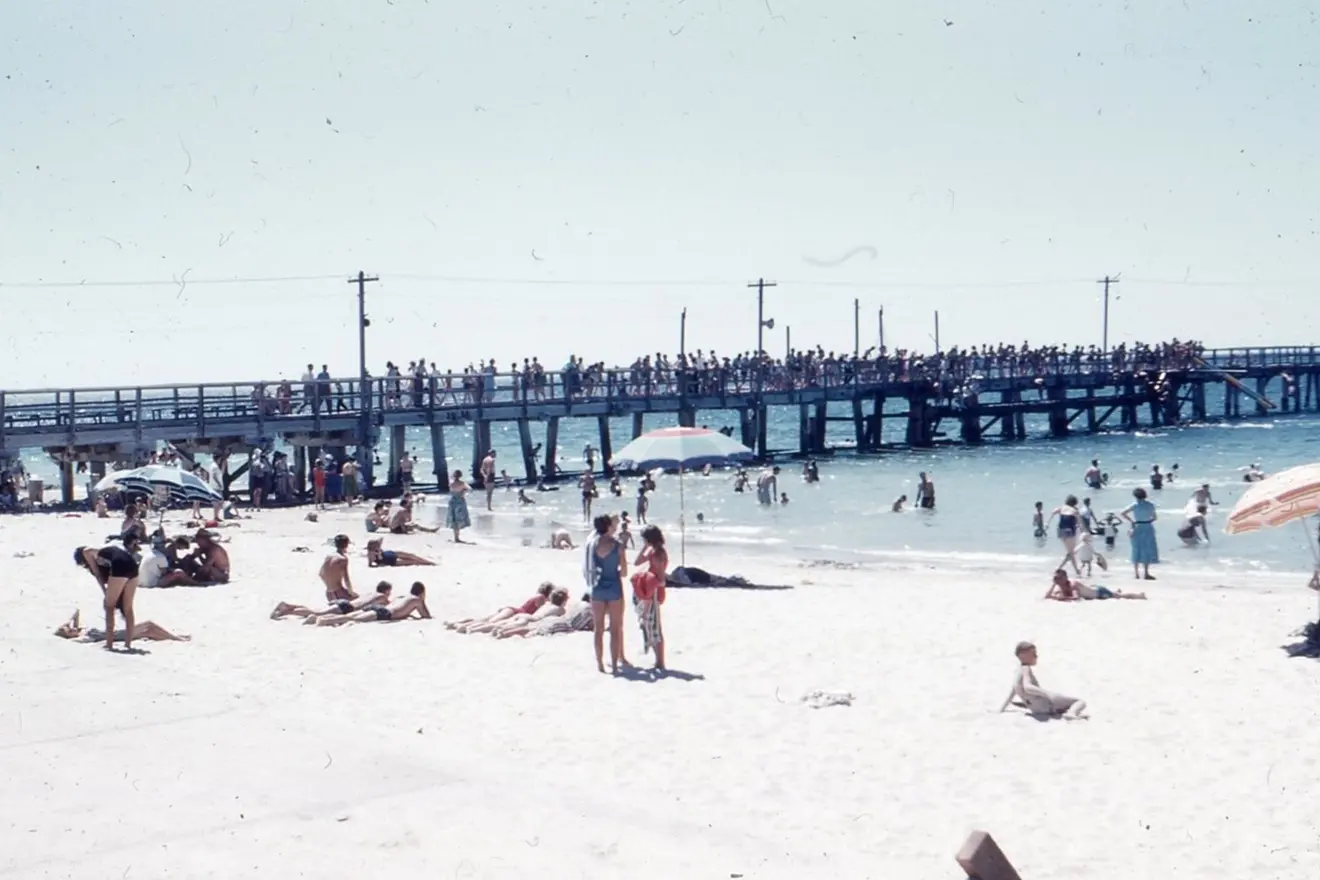 Photo of the Busselton Jetty taken circa 1960. It shows many people on the jetty and beach.