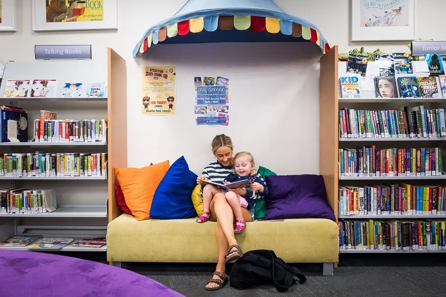 A woman sitting down and reading a book to a small child.