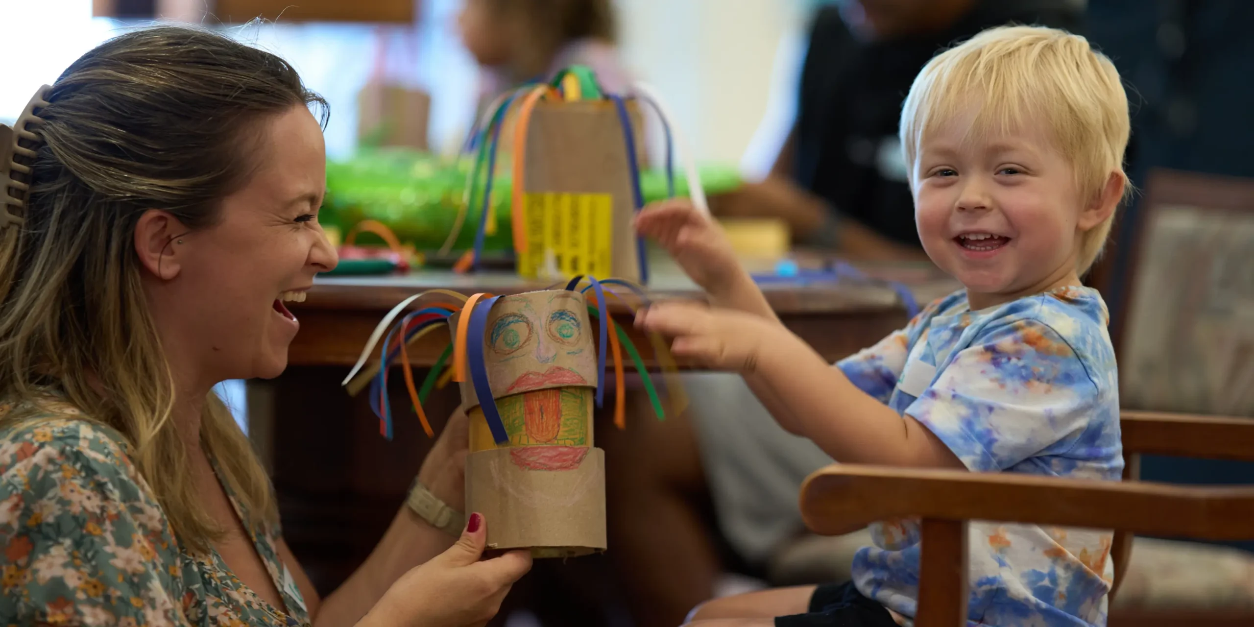 A toddler and their mother play with a hand-made craft puppet.