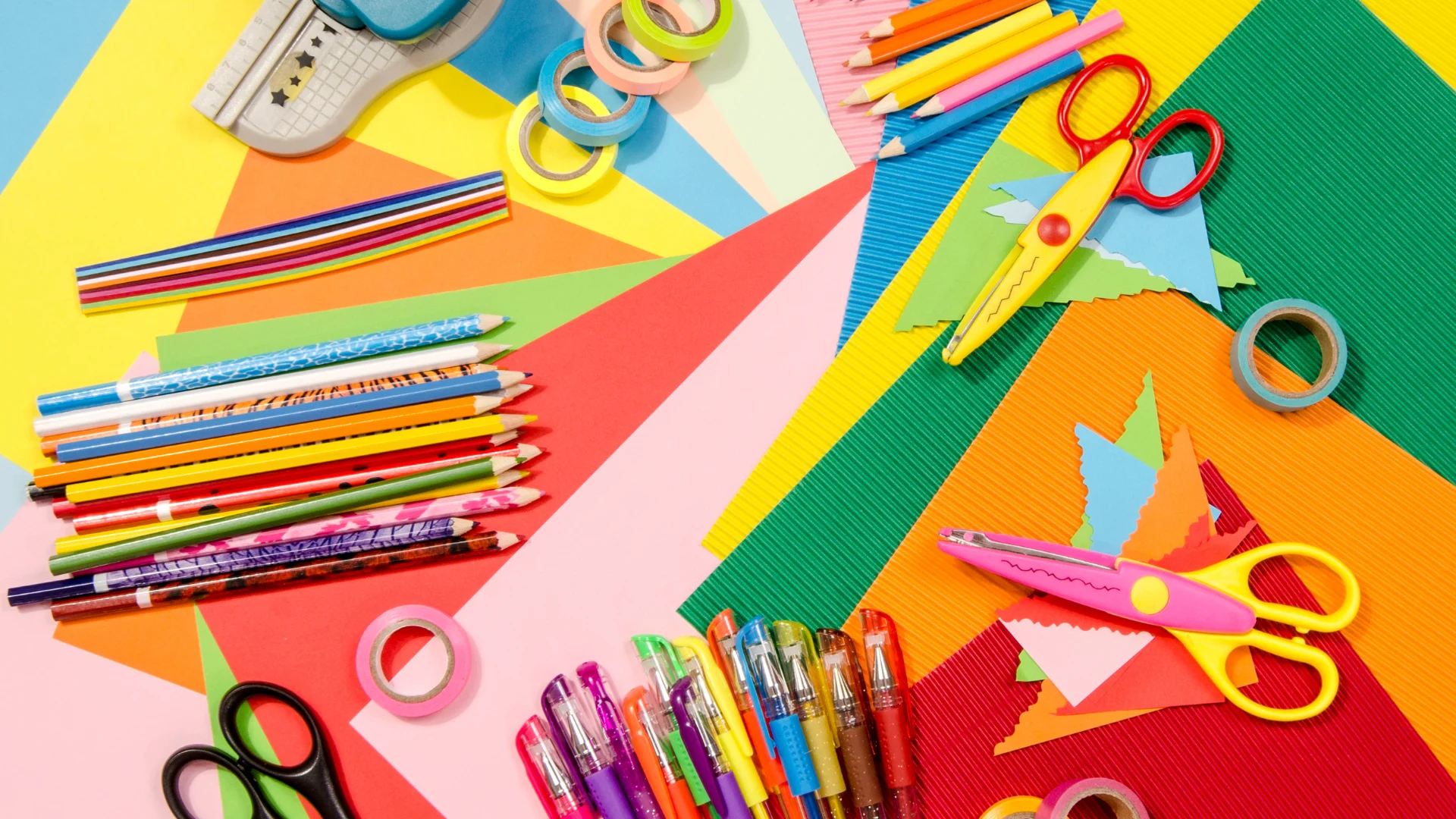 Pencils, scissors and other colourful craft items laying on coloured paper