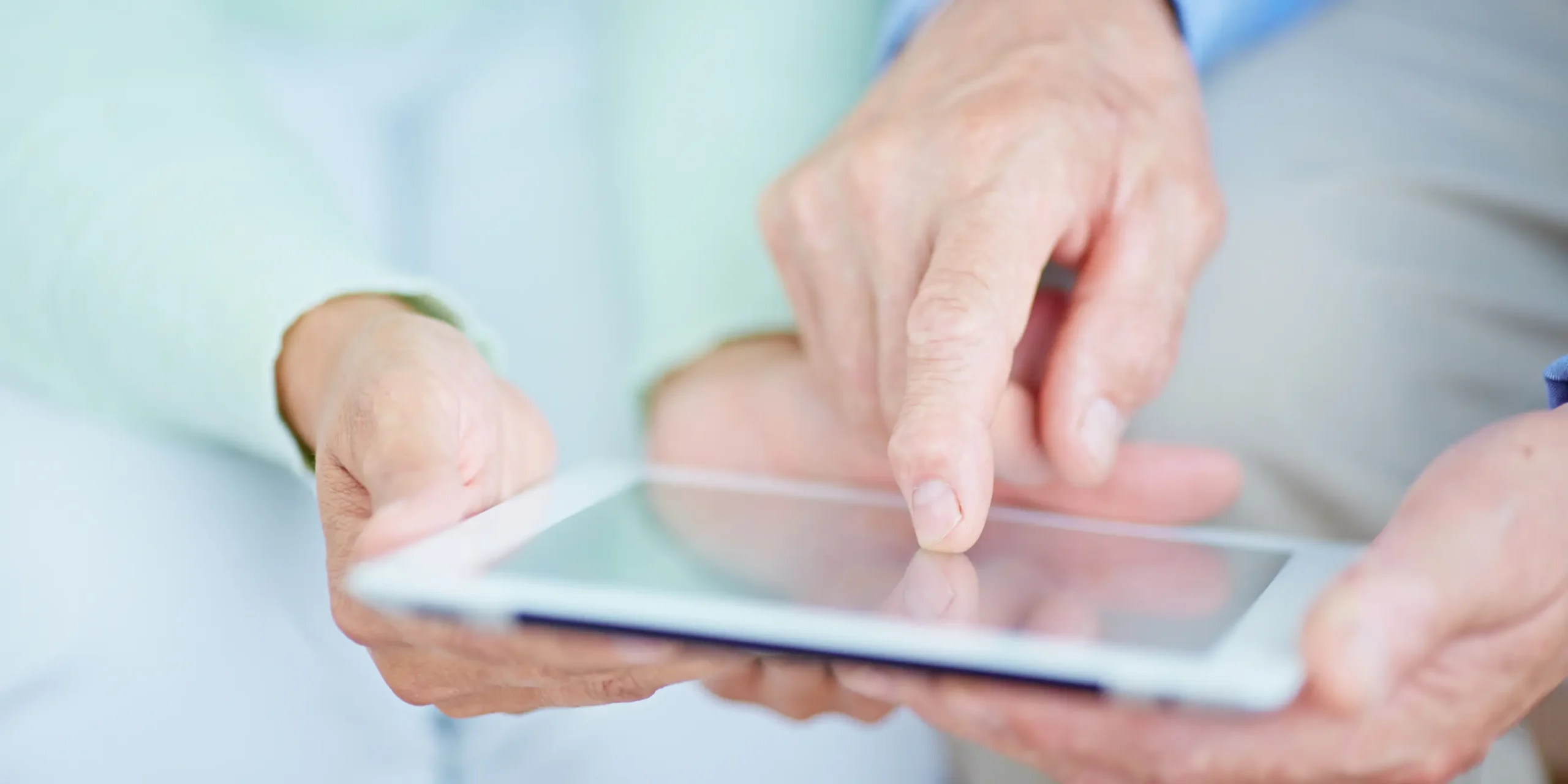 A close-up image of hands pointing to the screen of a tablet.