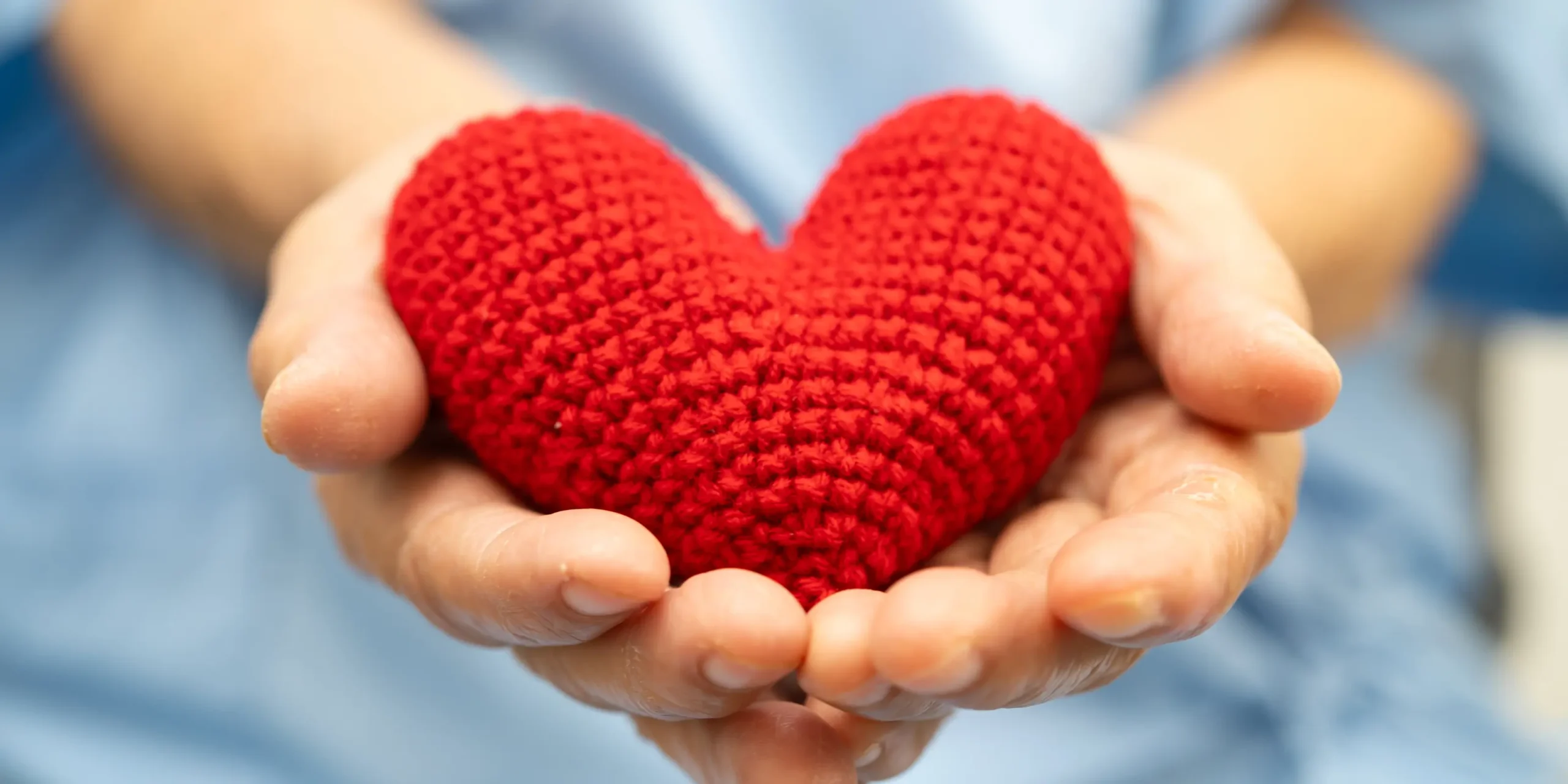 A close-up photo of hands holding a knitted love heart.