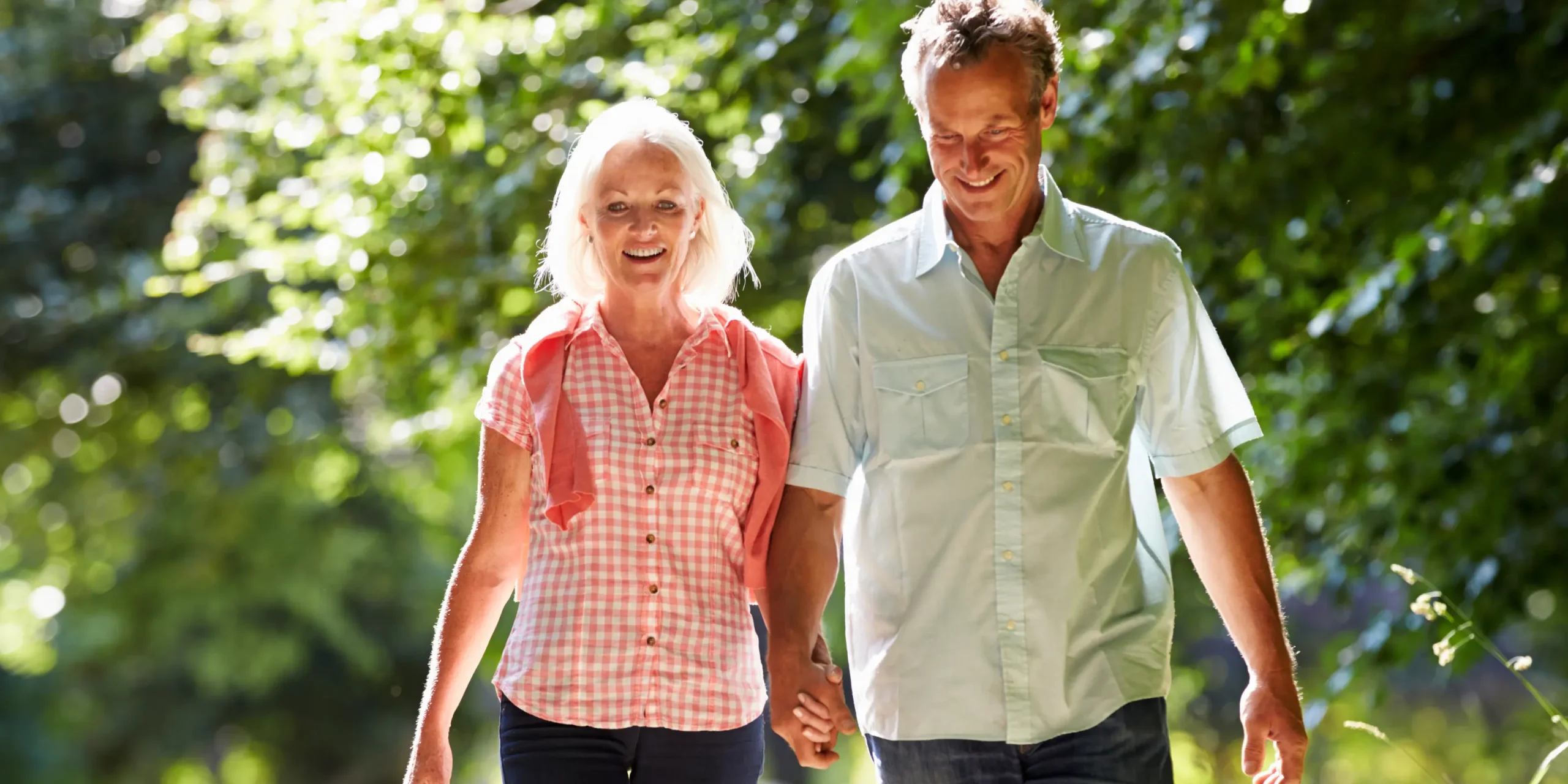 A man and woman in their 50s or 60s, walking hand-in-hand.