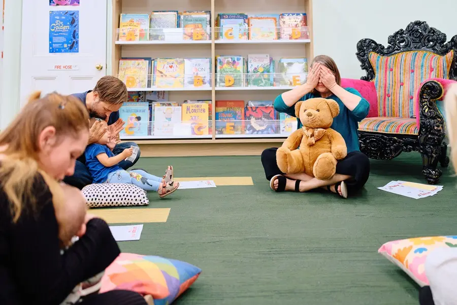 A woman with a teddy bear covering her eyes, while parents cover the eyes of their babies.