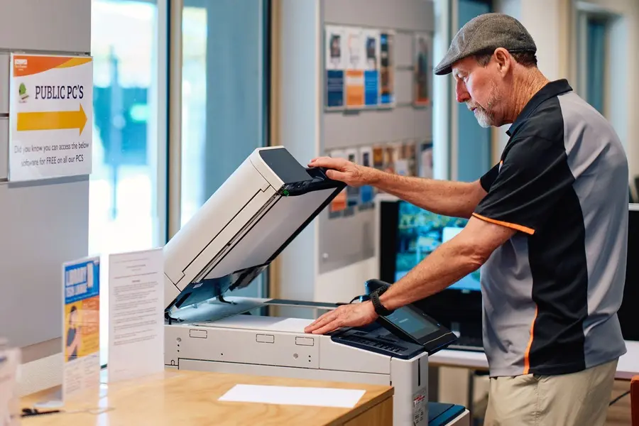 An older man wearing a hat operating a photocopier.