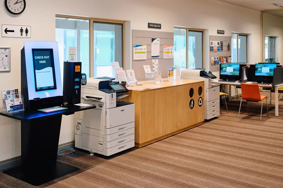 The inside of Busselton Library, showing a self-serve kiosk, printers, and PCs.