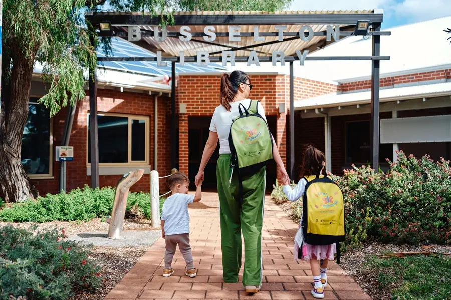 A woman holding the hands of two children as they all walk into Busselton Library.
