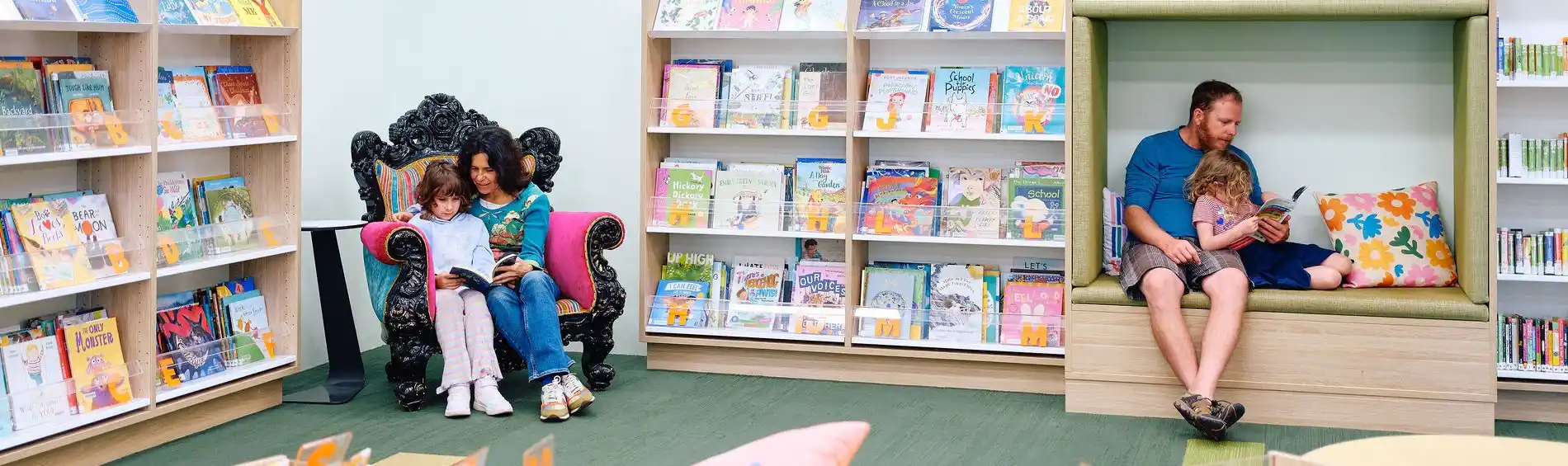 library-guidelines-2026 Two pairs of a parent and child sitting and reading a book together.